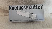 Front view of the Kactus Kutter box showing product name and features such as dual direction grind, strong torque power, patented sword-shaped disc, and anti-skid funnel.