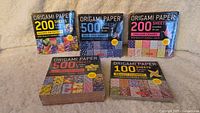 Five packs of origami paper laid out on a surface, showing variety of counts and patterns