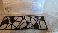 Top view of black metal wall hanging showing abstract curved and circular cut-out pattern on a flat surface.