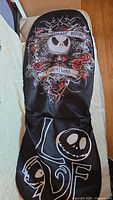 Full front view of one black car seat cover showing detailed Nightmare Before Christmas graphics including Jack Skellington face, roses, spiderweb, and LOVE design.