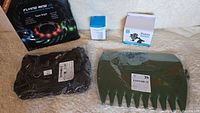 Photo of a black LED flying ring toy package, small white humidifier box, mobile phone holder mount box, large green plastic hand rake with wide teeth, and a black unknown item in plastic packaging