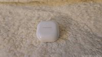 Closed white Samsung Galaxy Buds 2 charging case on light-colored textured surface.