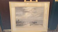 Framed coastal watercolour painting in muted colors, showing boats by rocky shore under cloudy sky, titled 'Morning Light'.
