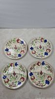 Set of four round divided plates arranged flat, showing floral hand-painted patterns and three divided sections each.