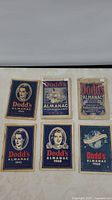 Photo showing the front covers of six Dodd's Almanac booklets dated from 1920s to 1960, various cover designs and colors.