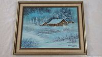 Framed oil painting of a winter cabin scene, showing the entire artwork and frame against a light background.