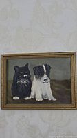 Framed early oil painting on cardboard featuring a black cat and a black and white dog seated next to each other.