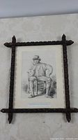 Full view of the handcarved wooden frame with the antique black and white printed portrait of a seated man.