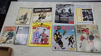 Nine hockey-related books and programs arranged on a table, showing variety of hockey topics and historical publications.