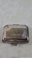 Closed rectangular silverplate candy dish with patent and brand markings on lid, showing overall shape and size.