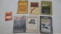 Seven antique hunting and gun related booklets laid out on a white surface, showing their front covers.