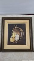 Framed still life oil painting showing pear, apple, silver plate, and walnuts on dark background
