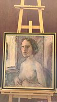Framed oil painting of a female nude bust placed on an easel. The painting is 27 x 24.5 inches and shows a figure with short hair against an abstract background.