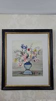 Full view of framed watercolour painting of floral bouquet in blue vase, mounted on wall.