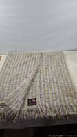 Full view of colorful wool throw with fringe edges laid flat showing folded corner and label.