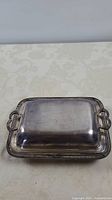 Photo of the silverplate covered side dish closed, showing rectangular shape, simple handles, and decorative edging on base tray