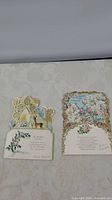 Two vintage Hallmark fold-out cards laid flat showing detailed cut and embossed designs, one Christmas-themed with deer, the other floral with blue background and pink heart.