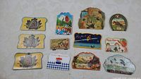 Nine vintage sewing needle booklets displayed on a white surface, showing front cover designs including animals, people, and landscapes.