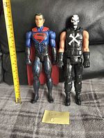 Front view of Superman and Crossbones action figures alongside a measuring tape showing approximate height of 12 inches.
