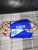 Close-up photo of rope bundle showing label indicating 20 feet length, wrapped in a blue and green paper label, lying on cloth background.