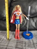 Barbie Supergirl doll posed sitting with ruler for scale and stand included
