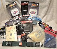 Overview photo showing multiple baseball and umpire accessories including wristbands, belts, umpire clickers, and hip ball bags, all sealed or with tags