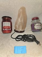 Photo showing large salt lamp with electrical cord in center, flanked by two glass jar candles (red on left, purple on right) with Lot P note.
