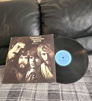 Photo of the vinyl record next to the album cover showing front cover artwork with black and white photo of band members.