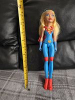 Full body photo of the Supergirl doll standing upright next to a ruler measuring about 12 inches.
