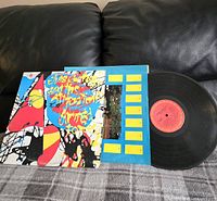 Album cover sleeve with colorful abstract artwork on a gray blanket on couch.