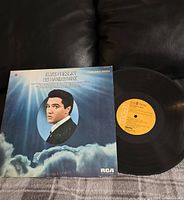 Photo showing the front album cover of 'His Hand In Mine' by Elvis Presley, depicting a large photo of Elvis in front of clouds and sky.