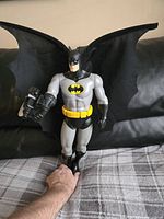 Front view of Batman figure with batwings spread open, displayed on couch with hand for scale.