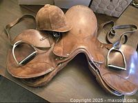 Top-down and side angled views of the brown leather Johs. Stübben Krefeld youth saddle with attached stirrups and vintage velvet riding helmet.