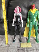Front view of Ghost Spider and Vision figures standing next to measuring tape showing approx 12 inches tall.