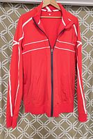 Front view of men's lightweight Lululemon jacket in red with white stripe accents, full zip, and pockets.