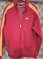 Front view of new men's medium Nike athletic jacket in red with orange stripes and yellow Nike swoosh logo on chest.