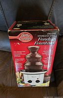 Front view of the boxed Betty Crocker Deluxe Stainless Steel Fondue Fountain showing product image and branding.