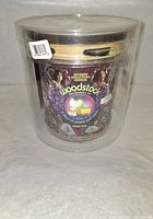 Front view of the sealed Woodstock 4-disc DVD set with the tambourine on top inside a clear plastic cylindrical case. The packaging shows colorful artwork and the title 'Ultimate Collector's Edition Woodstock The Director's Cut 4-Disc DVD'.