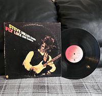 Vinyl record displayed alongside the 'Fly Like An Eagle' cover sleeve showing Steve Miller playing guitar.