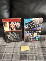 Photo showing two paperback books on a dark surface. The books are 'Read Between My Lines' by Sandra Halliburton, about Stevie Nicks, and 'Black Market Beatles' about The Beatles.