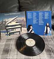 Vinyl record slightly out of sleeve with cover visible behind showing artwork of grand piano in snowy mountain setting and band members on back.