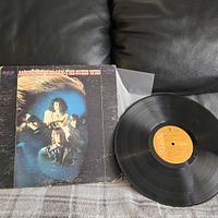 Vinyl record of "American Woman" by The Guess Who in original sleeve with band photo and album title visible, placed on dark surface.