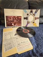 Photo showing record, open album jacket with group hands image, and printed inserts in folder.
