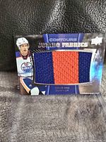 Front view of the Upper Deck trading card featuring Taylor Hall with a large two-color fabric swatch patch in orange and blue from Edmonton Oilers jersey.