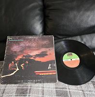 Photo of Genesis album cover and vinyl record on black surface showing front cover artwork and record condition.
