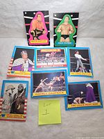 Photo shows a collection of 7 vintage WWF WWE items including 2 wrestler stickers and 5 trading cards. Stickers are bright pink and green featuring Brutus Beefcake and Ivan Putski. The trading cards are bordered in blue and yellow with various wrestlers and match scenes including Wrestlemania III.