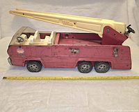 Side view of vintage 1970s Tonka metal firetruck showing the red body, six wheels, Tonka logo sticker, cream-colored extendable ladder, and molded white interior seats with clear windshield.