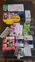Photo displaying multiple packs and boxes of assorted lightbulbs of various types and wattages on a surface.