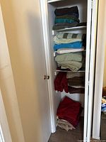 View of large bath towels stacked on several shelves in a closet space. Colors include dark brown, teal, green, blue, beige, red, gray, and tan.