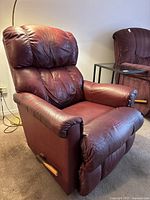 Front view of burgundy leather recliner showing cushioned seat, headrest and armrest, visible wear on leather.